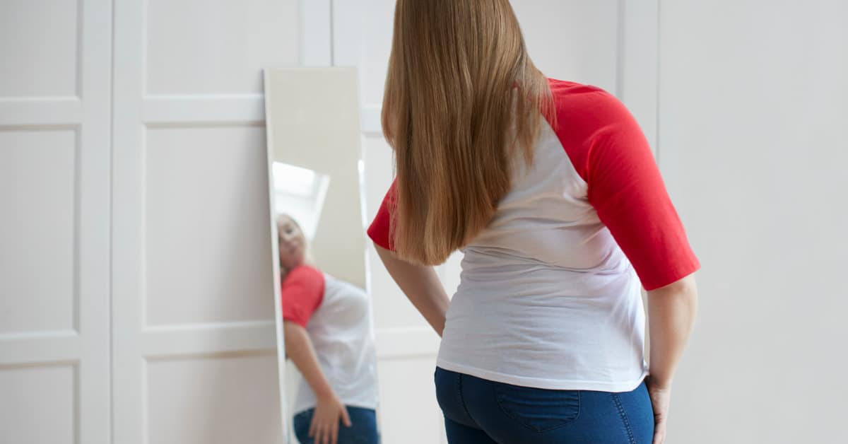 a woman looks at herself critically in the mirror